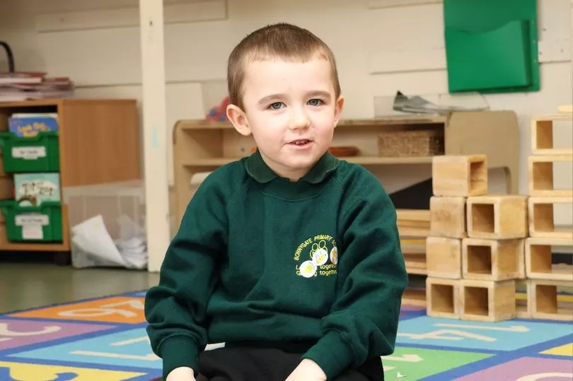 Lincoln Brookes, a young boy with autism, in a green sweatshirt sitting in a classroom.