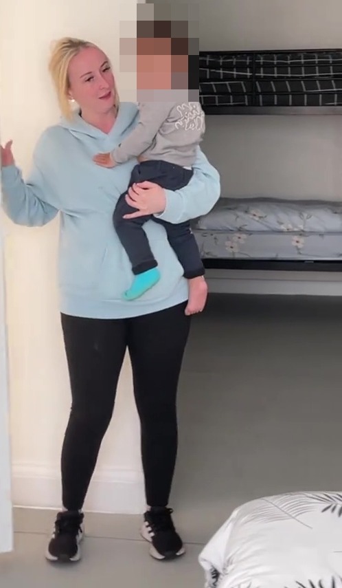 A mother holding her child in an empty room with bunk beds, showing the impact of homelessness.