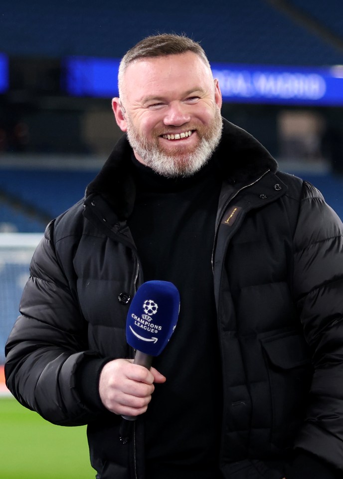 Wayne Rooney smiles while holding a UEFA Champions League microphone.