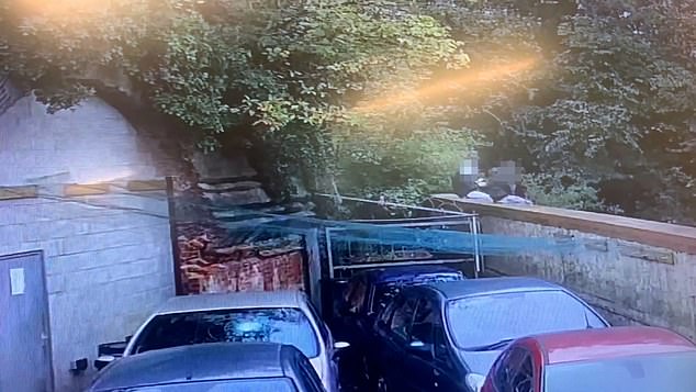 Two teens sit on a wall overlooking the garage, next to a damaged car