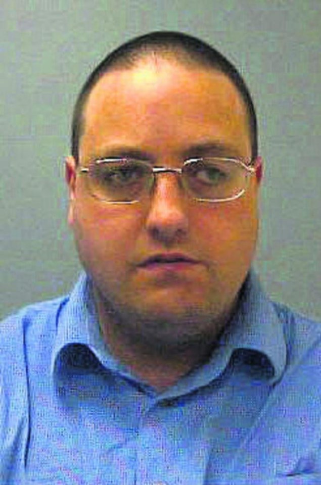 Mugshot of a light-skinned man with closely cropped dark hair and glasses, wearing a blue collared shirt.