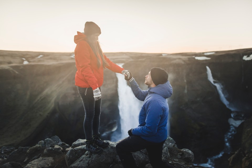 Young man proposing to his girlfriend while hiking by a waterfall.