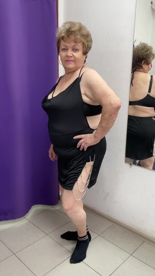A woman in a black mini-dress with chain details posing in front of a mirror.