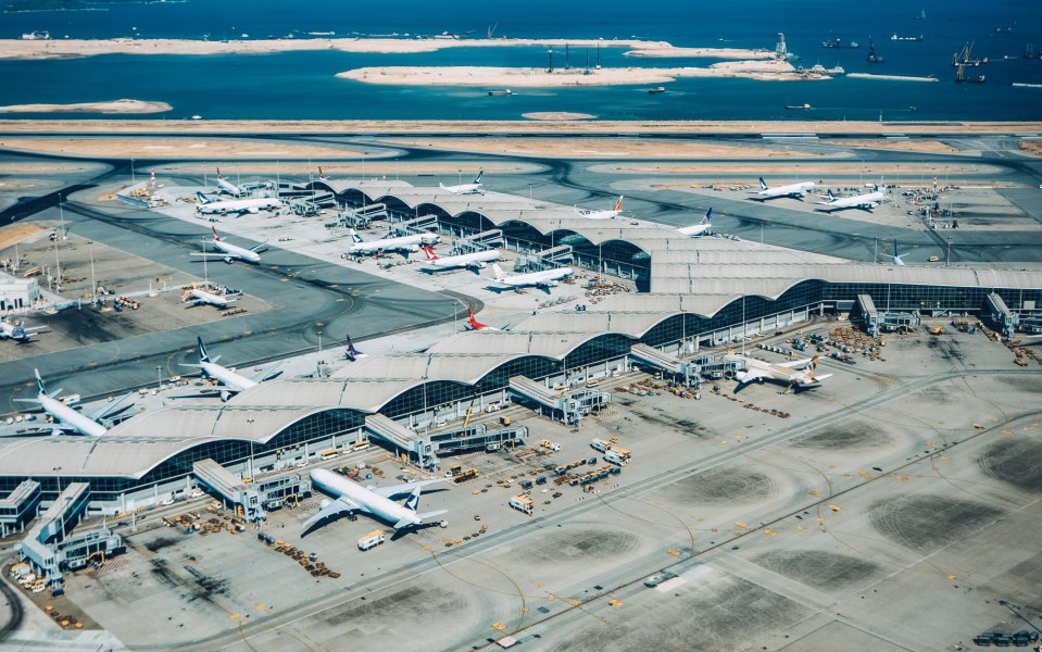 Aerial view of an airport terminal with many parked airplanes and a body of water in the background.