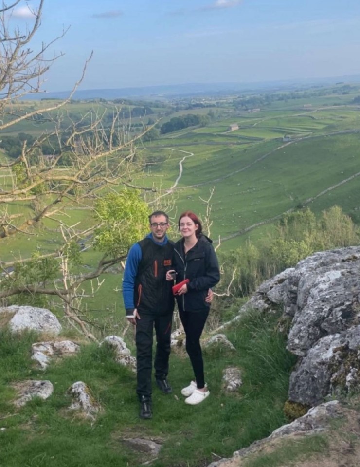 Two people posing for a photo on a rocky hill overlooking a vast green valley.