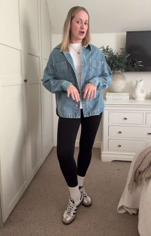 A woman in a blue denim jacket over a white t-shirt and black leggings with white socks and sneakers.