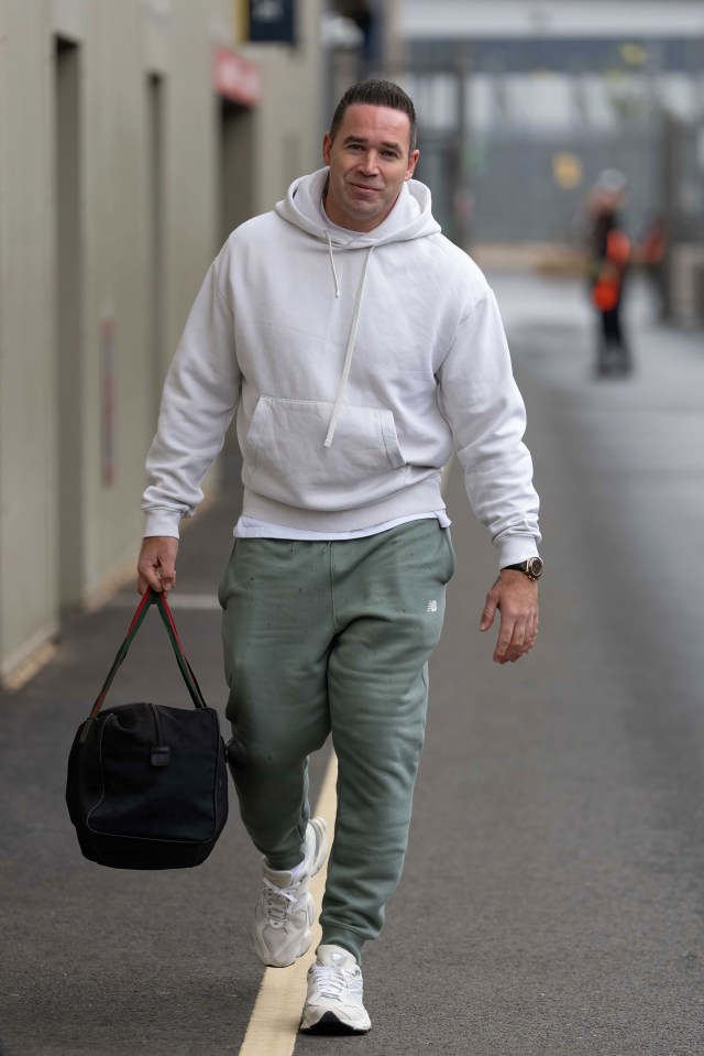A man in a green t-shirt with a letter R on it, gestures with his left hand while speaking.