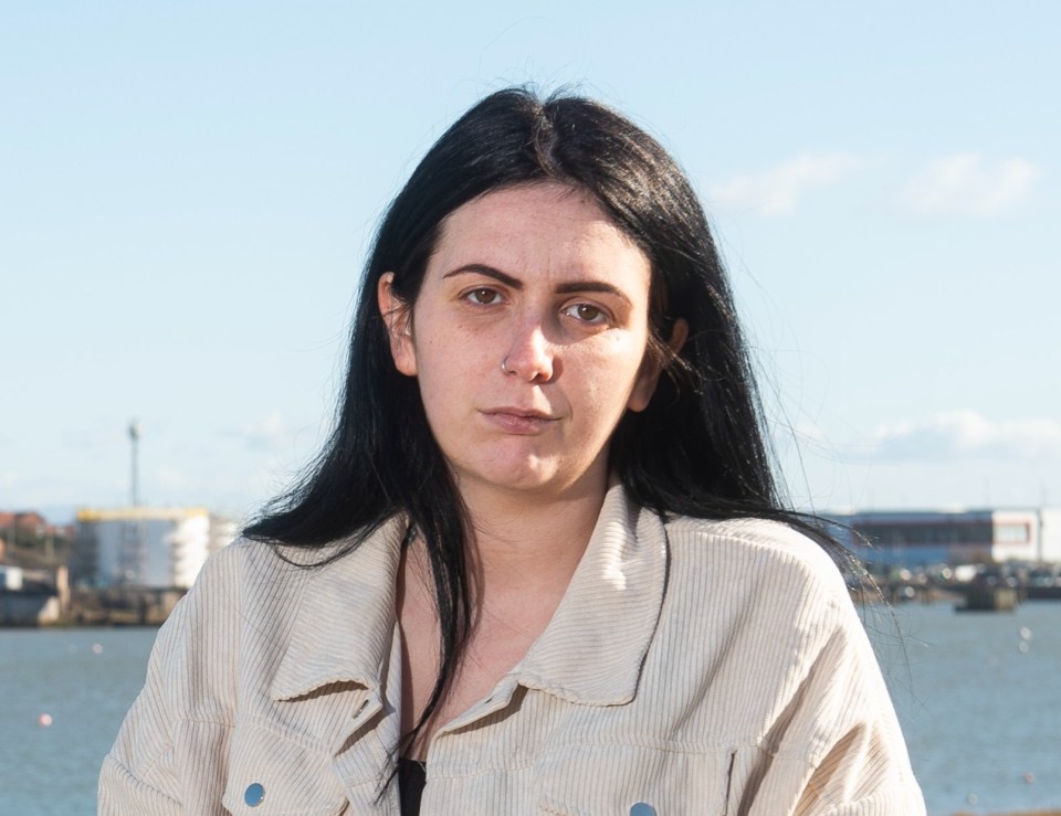 Ellie Reynolds, a young person, sits in front of a river, boats, and buildings.