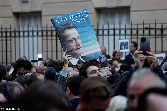 A supporter holds a poster with a portrait of Nicolas Sarkozy and the slogan 'Strong France' as people attend a gathering called by the sons of the former French President