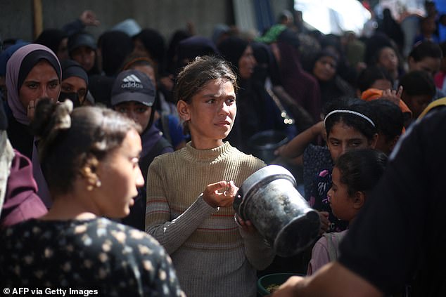 Displaced Palestinians gather to receive food portions from a charity kitchen in the Nuseirat refugee camp, located in the central Gaza Strip, on Tuesday