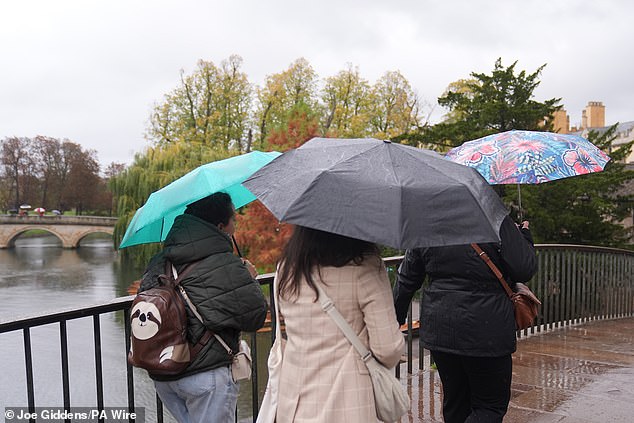 People shelter from the rain under umbrellas on Garret Hostel Bridge in Cambridge on Monday