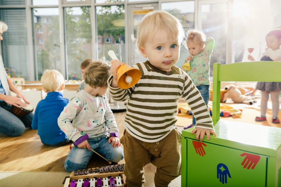 Toddler ringing a bell in a preschool music room.
