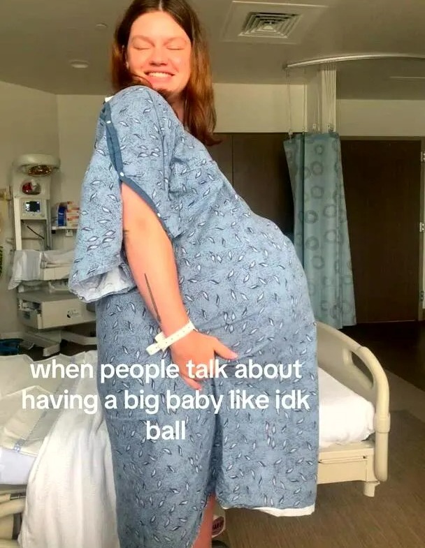 A woman in a hospital gown holding her very large pregnant belly.