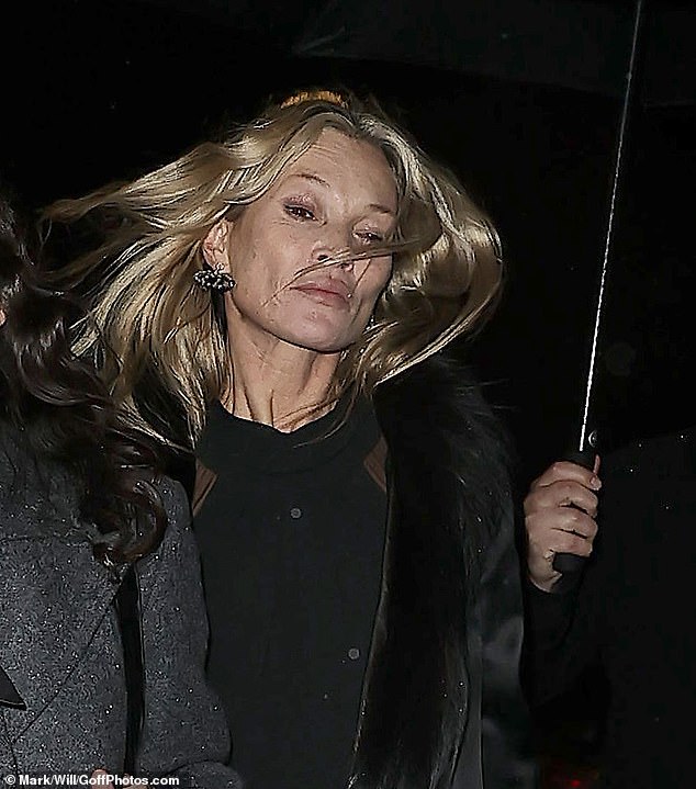 Her loose hair was caught in the wind while an aide covered her with an umbrella