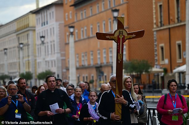 A pilgrim holds a cross at Vatican City today as he awaits the arrival of the King and Queen