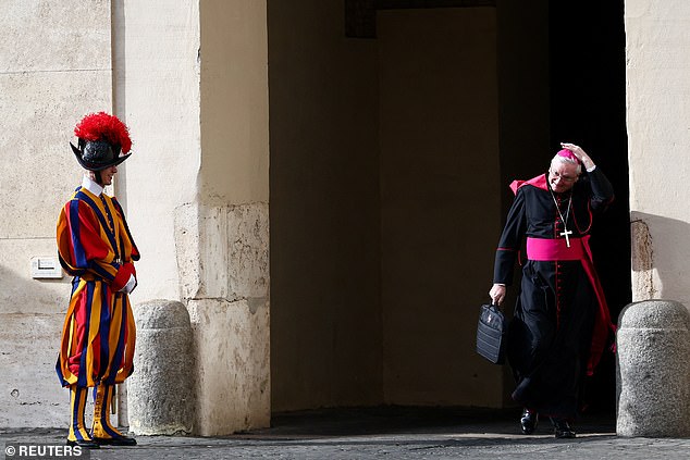 A clergy member adjusts his zucchetto next to a Swiss Guard at Vatican City this morning