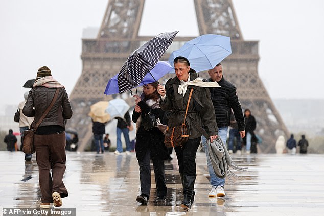 People walk in the rain during the 'Benjamin' storm with the Eiffel Tower in the background in Paris on october 23, 2025