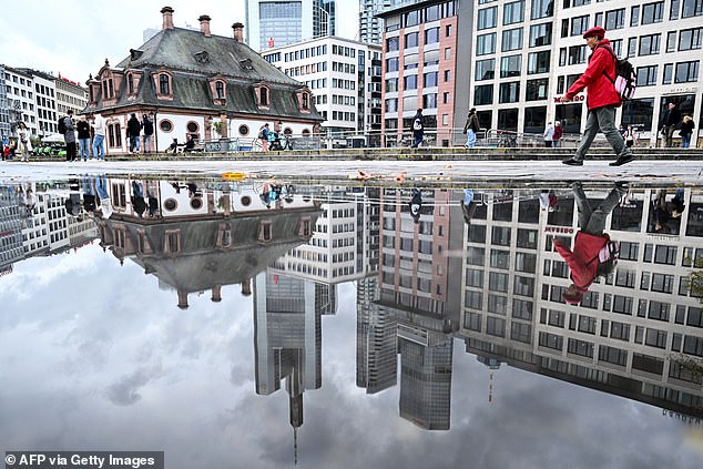 A woman is reflected in a puddle as she walks outside the banking district in Frankfurt am Main, western Germany, on October 23, 2025