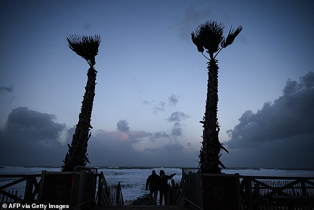 A man and a woman look at waves as storm Benjamin is causing 'strong gusts' in Lacanau, south-western France, on October 23, 2025