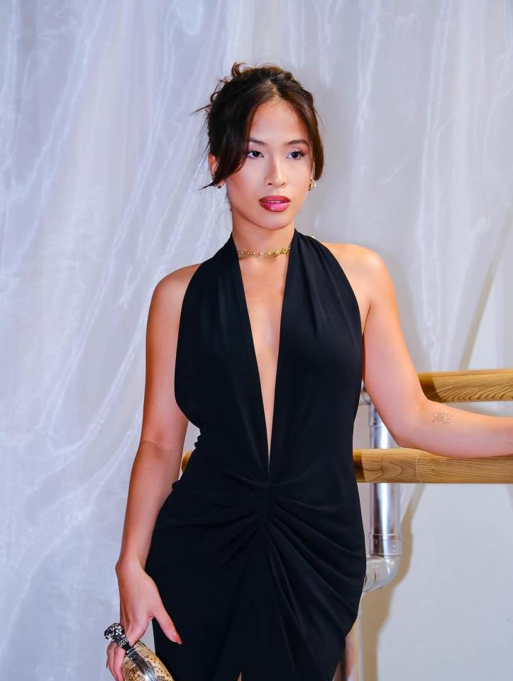 Woman in a black halter dress holding a clutch, leaning against a ballet barre.