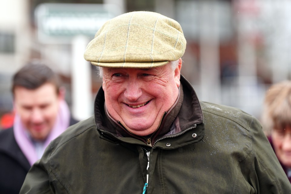 Trainer Paul Nicholls smiling while wearing a flat cap and olive green jacket at Taunton Racecourse.
