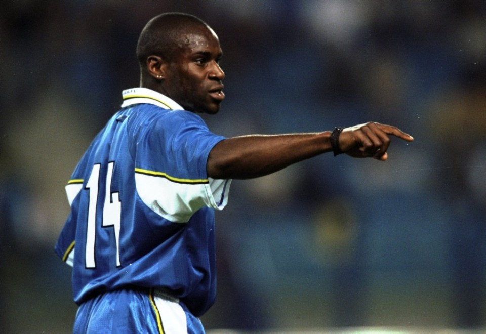 Frank Sinclair wearing a blue and white football jersey, pointing to the right.