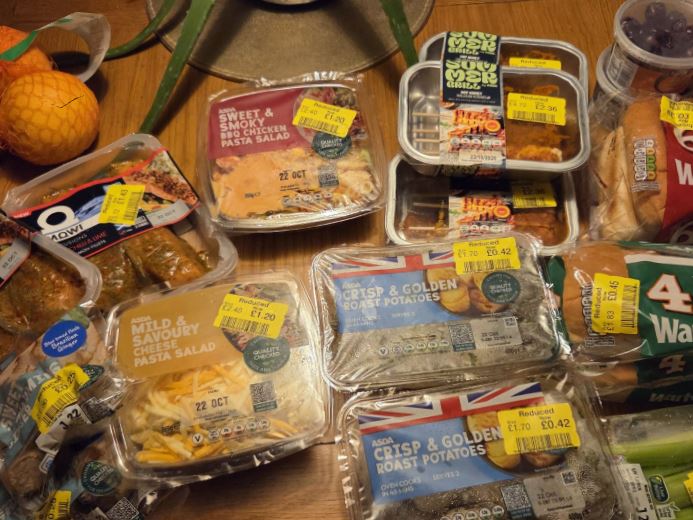 Various supermarket reduced-price food items including pasta salads, roast potatoes, and grilled meat, all with yellow "reduced" stickers.