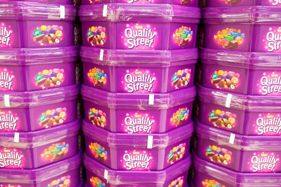 Quality Street chocolate tubs stacked on a supermarket shelf.