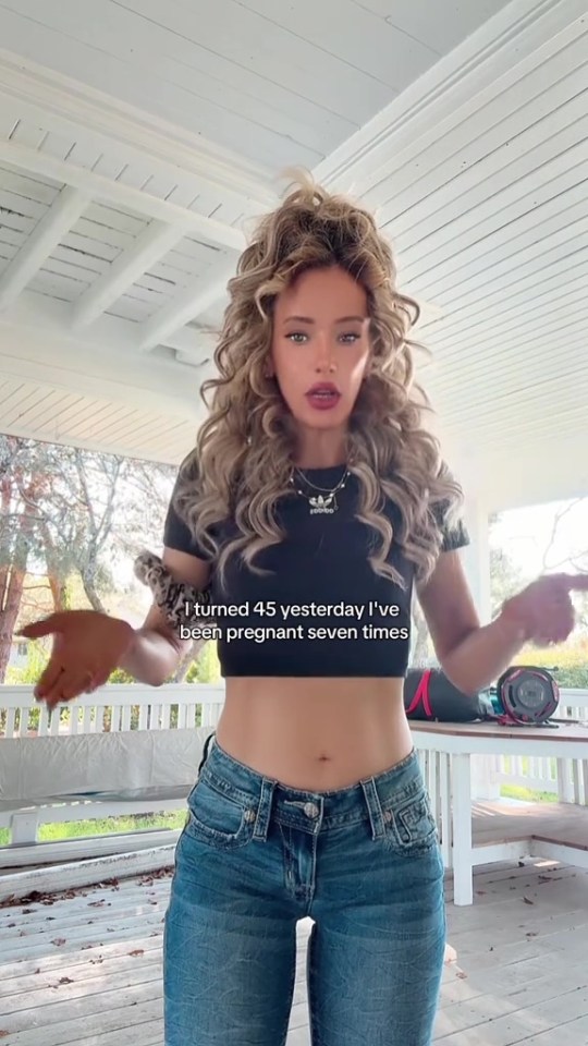 A woman with long curly hair wearing a black crop top and jeans, with text stating "I turned 45 yesterday I've been pregnant seven times".