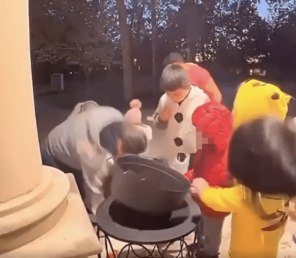 Parents emptying a trick-or-treat bucket while children in costumes watch.