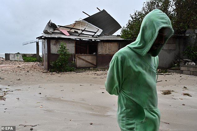 A man walks by a house damaged by the winds of Hurricane Melissa at Hellshire Fishing Beach