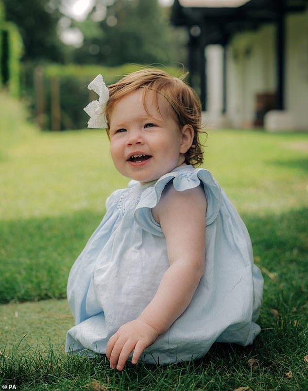 Lilibet is seen wearing a pale blue frock with a white bow in her reddish locks while she sat in the grass during her first birthday party in 2022