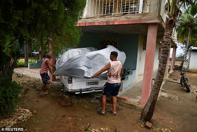 Men were pictured attempting to protect their cars and belongings ahead of Hurricane Melissa's arrival in Cuba on Wednesday morning