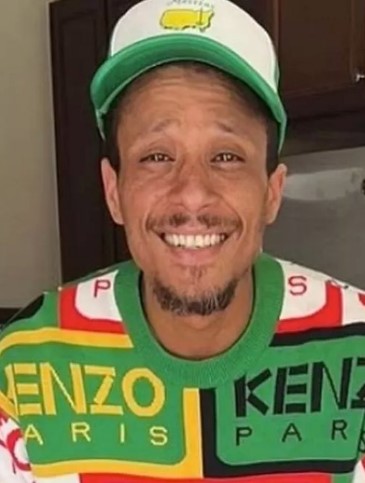 Floyd Roger Myers Jr. smiling and wearing a green and white Masters hat and a colorful Kenzo sweater.