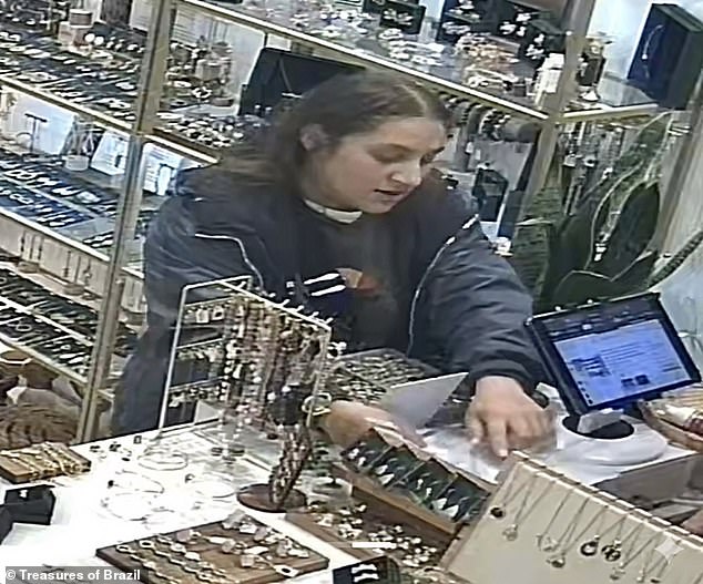 The woman takes a small piece of paper from her pocket and places it on the counter which she then uses to hid her movements as she steals the two phones