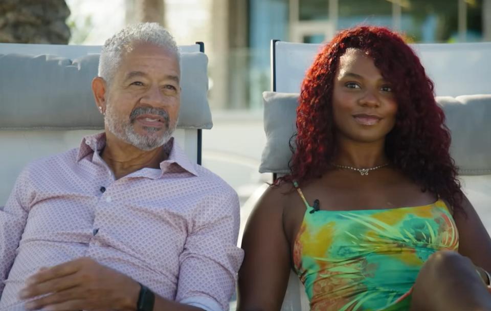 A man with gray hair and a woman with red hair sit on lounge chairs.