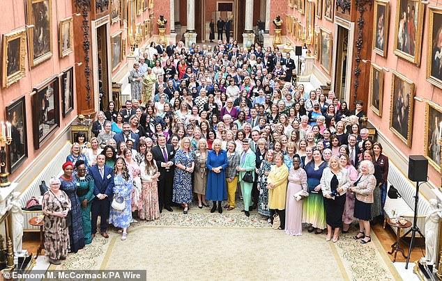 Queen Camilla poses for a photo with guests at a reception to mark the relaunch of the Wash Bags project, at Buckingham Palace, in May 2024