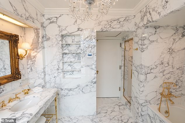 The new bathroom features a large bath tab and separate enclosed shower with golden faucets, railings, soap dishes, coat hooks and lamps, which are accented on bright marbled walls and floor