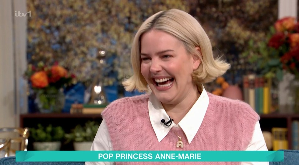 Anne-Marie, wearing a pink sweater vest over a white shirt, laughing on ITV1.
