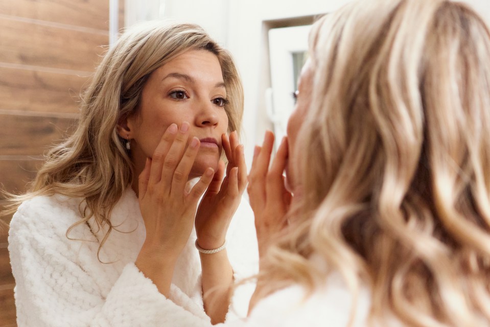 Woman in a bathrobe analyzing her skin in a mirror.