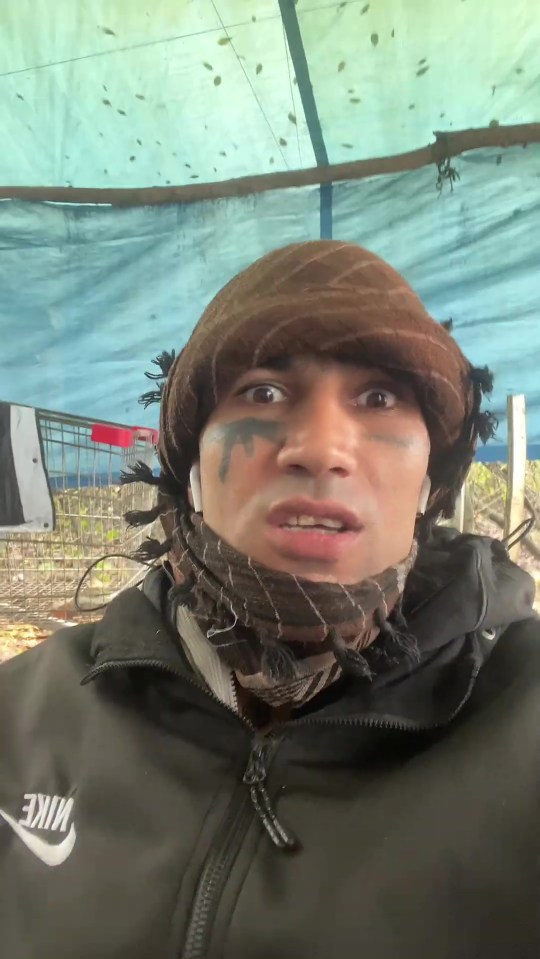 A man wearing a brown head covering and a black scarf around his neck with black face paint under his eyes.