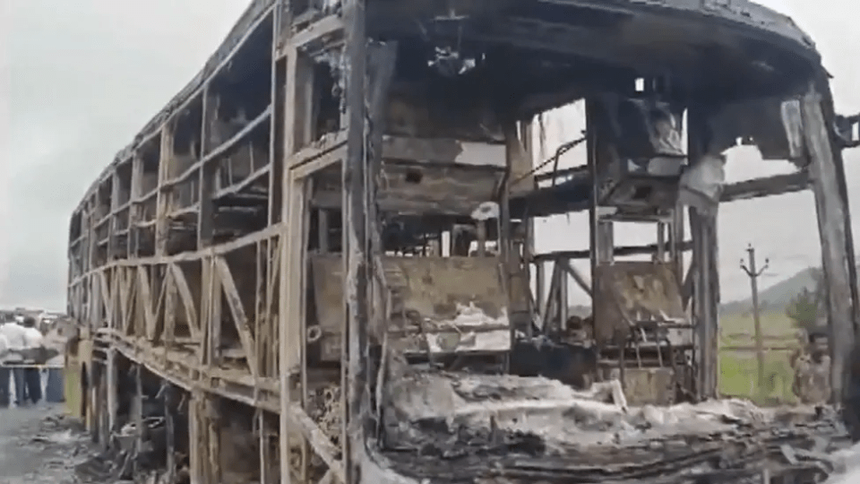 Remains of a burned-out bus, charred to its skeletal frame, are seen from the side and front.