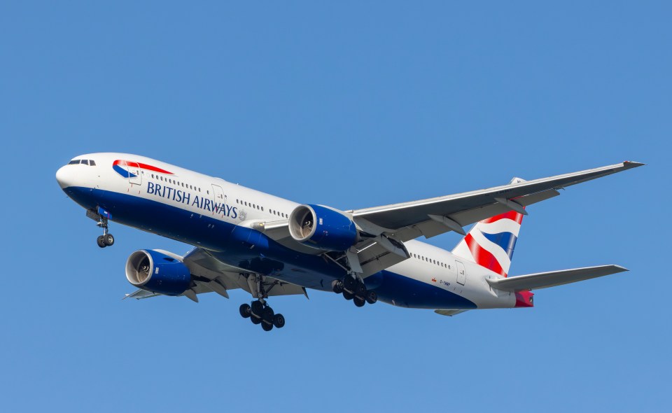 British Airways Boeing 777-200 aircraft landing with landing gear extended against a clear blue sky.