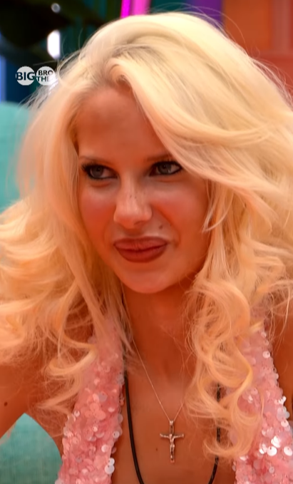 A blonde woman with blue eyes, freckles, and a pink sequined top wearing a crucifix necklace.
