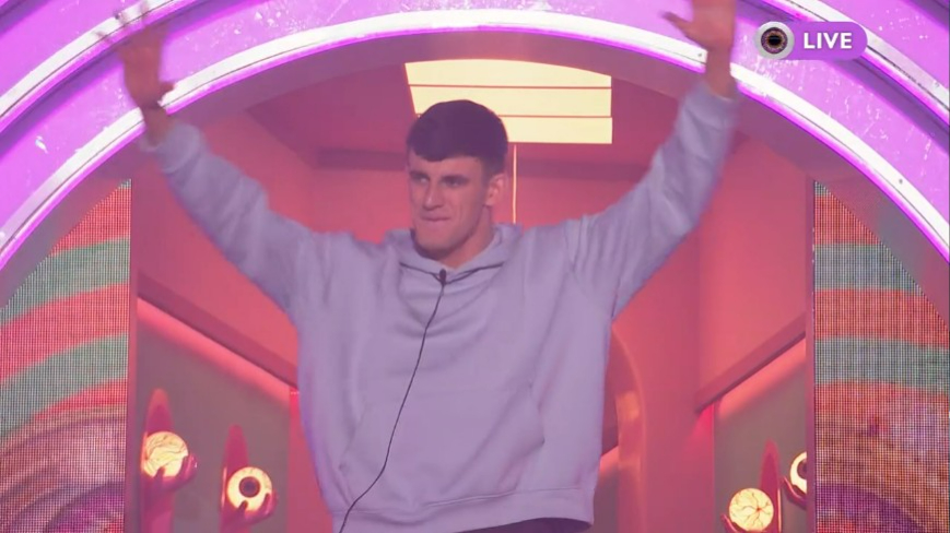 Big Brother star Cameron B with his arms raised, shouting "bulls***".