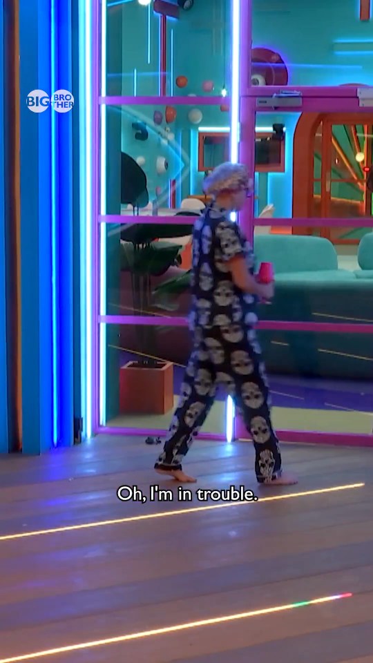 Caroline from Big Brother wearing skull pajamas and holding a red cup, walking barefoot.