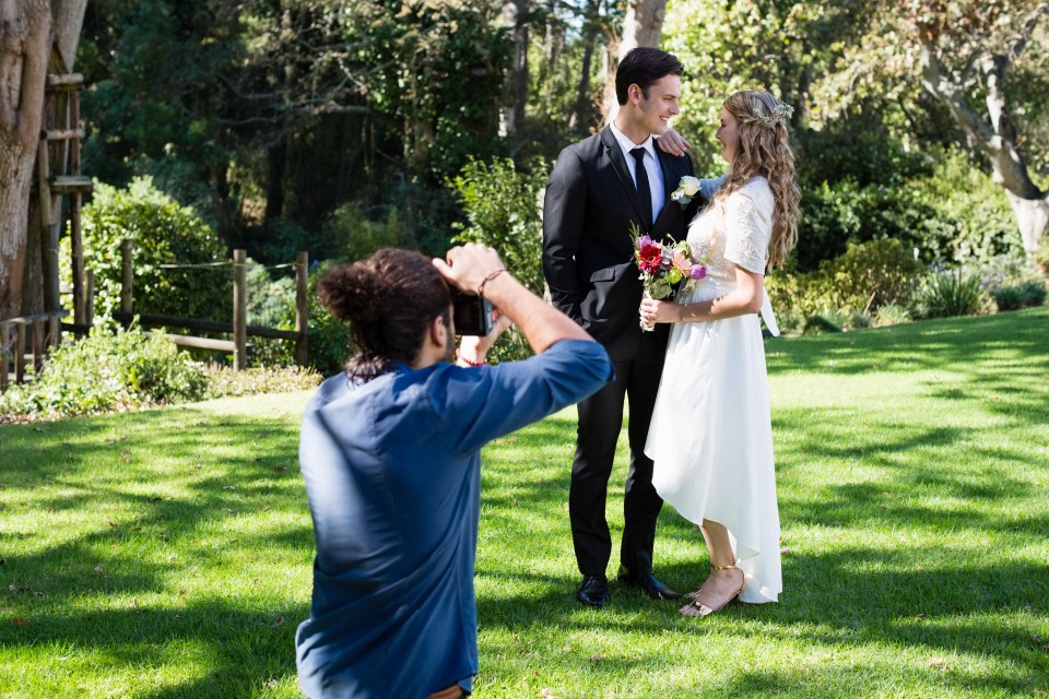 Photographer taking a photo of a newly married couple in a park.
