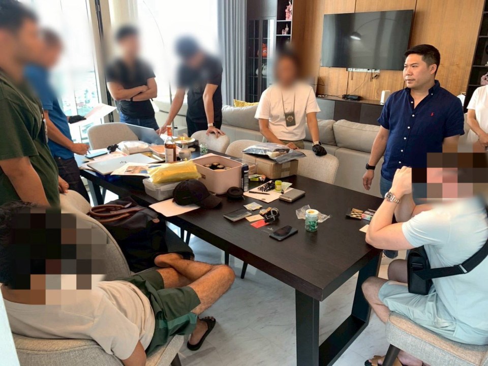 Police personnel and suspects gather around a table with alleged drug packages.