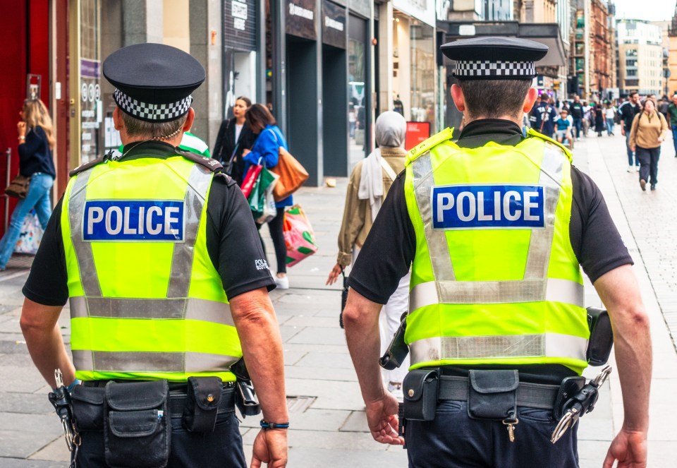 Rear view of two police officers in fluorescent vests walking on a city street in Glasgow.