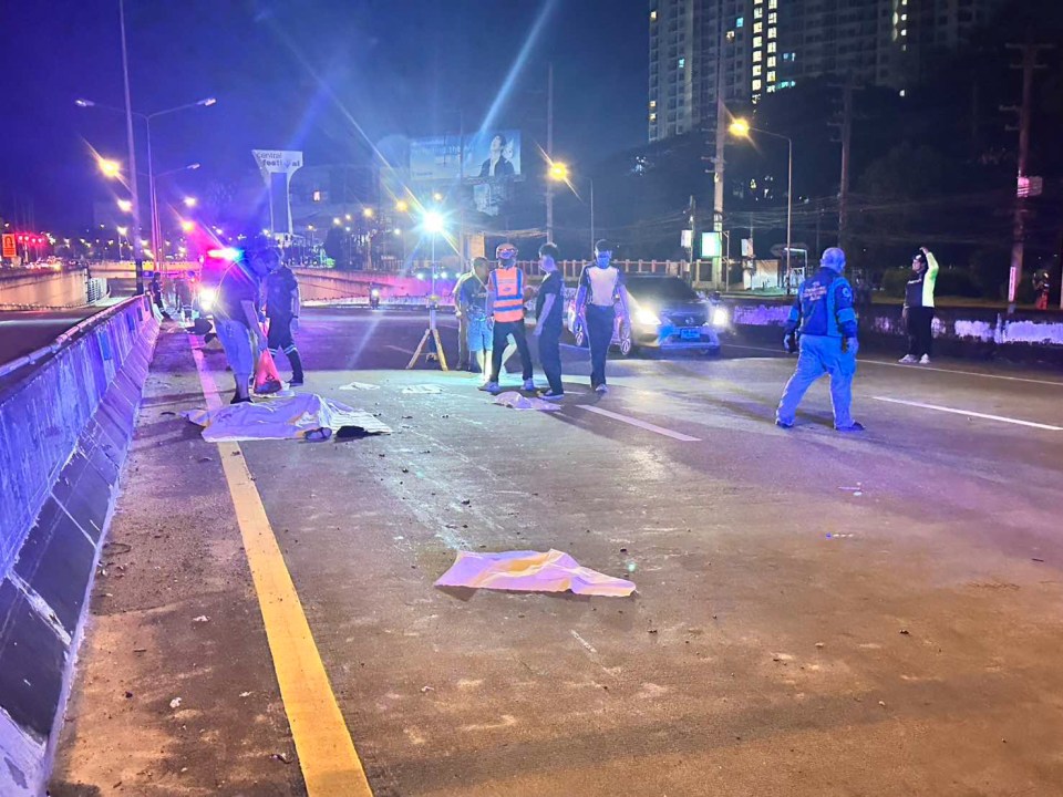 Crime scene of a motorbike crash on a highway at night, with several paramedics and police officers standing near body bags.